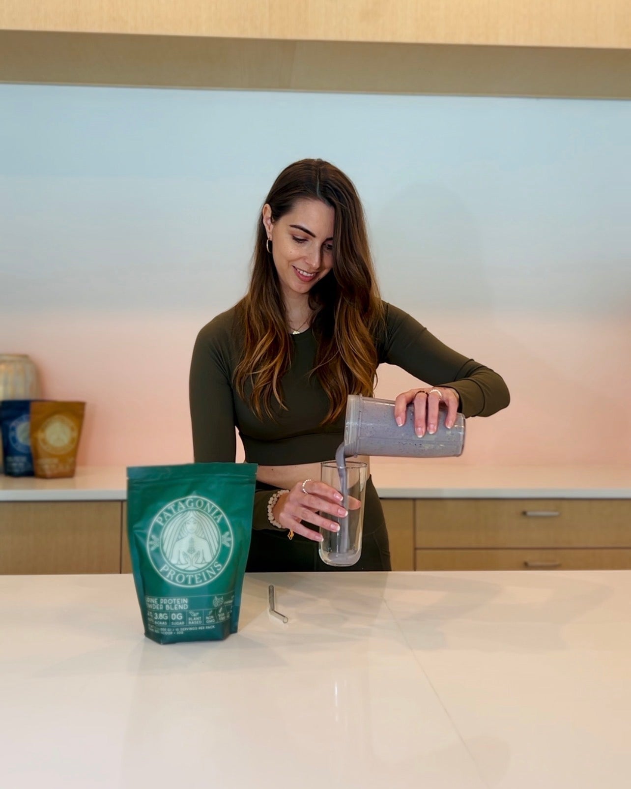 
                  
                    A woman in a kitchen setting pours Patagonia Proteins Inca Cherimoya Vegan Lupine Protein Smoothie from a clear plastic shaker bottle into a clear glass. A green bag of Patagonia Proteins Inca Cherimoya Vegan Lupine Protein sits on the white countertop in the foreground.
                  
                